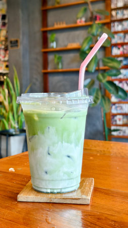 A chilled matcha latte with a pink straw on a wooden table, surrounded by plants and a cozy cafÃ©...