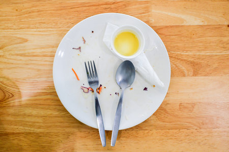 A white plate with fork and spoon on a wooden table, symbolizing a completed meal.の写真素材