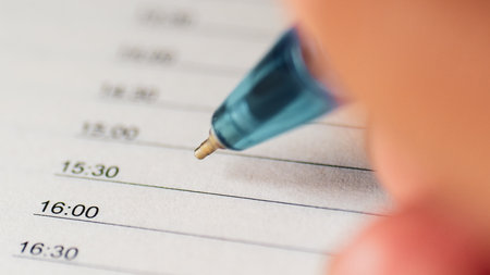 A detailed view of a hand using a blue pen to write in a planner, focusing on time management and organization.の写真素材