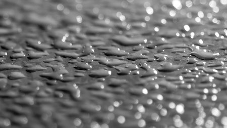 Black and white close-up of water droplets on a surface with a bokeh effect, creating a textured and reflective abstract background.の写真素材