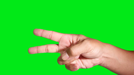 Close-up of a hand making a peace sign against a bright green background, symbolizing peace and victory.の写真素材