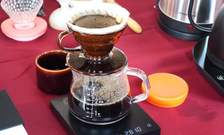 Close-up of pour over coffee brewing in a glass carafe on a digital scale, showcasing a cozy cafe atmosphere.の写真素材
