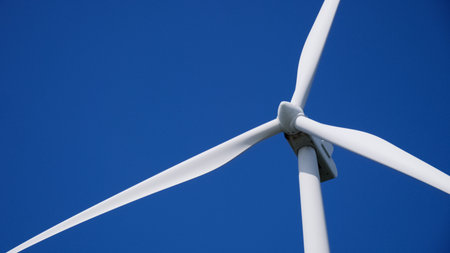 A wind turbine with blades set against a vibrant blue sky, symbolizing clean energy and sustainability.の写真素材