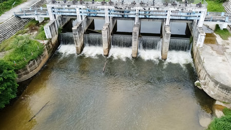 Aerial shot of water cascading through dam gates surrounded by greenery, showcasing engineering and nature.の写真素材