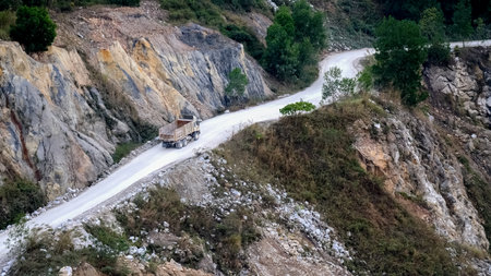 Truck travels on a winding mountain road surrounded by rocky cliffs and greenery, showcasing rugged natural beauty.の写真素材