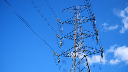 Steel transmission tower with power lines stretching across a vibrant blue sky, showcasing modern infrastructure.の写真素材