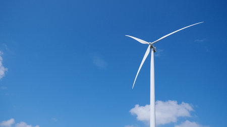 A single wind turbine stands tall against a vibrant blue sky, symbolizing clean and sustainable energy.の写真素材