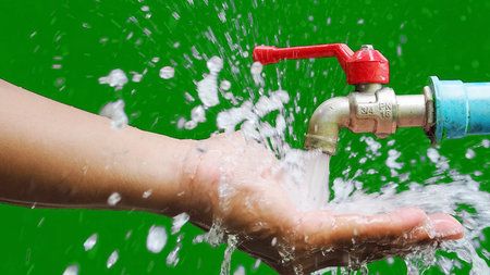 Hand washing under a running tap with splashing water, set against a vivid green backdrop.の写真素材