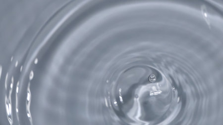 Detailed image of a single water droplet causing ripples on a smooth surface, captured in monochrome.の写真素材