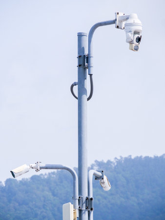 Modern surveillance cameras mounted on a pole, set against a clear sky and mountain backdrop, showcasing security technology.の写真素材