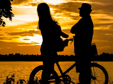 Silhouettes of a happy family with dogs and their bikes. . At the edge of the river, the sun shines.の写真素材