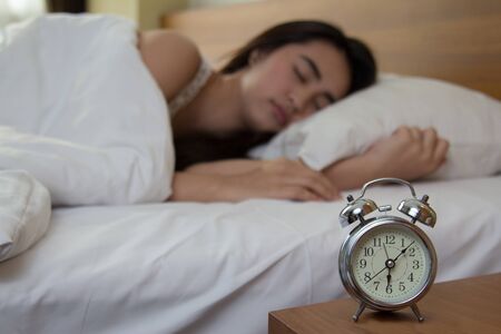 woman asleep in bed while her alarm shows the early time at home in bedroomの写真素材