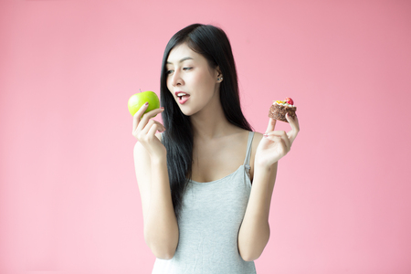 Beautiful young woman making a choice between a cake and appleの写真素材