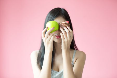 Beautiful young woman making a choice between a cake and appleの写真素材