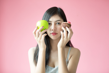 Beautiful young woman making a choice between a cake and appleの写真素材