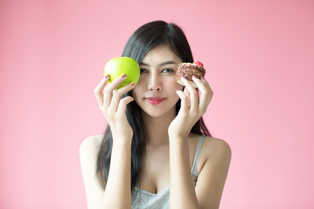 Beautiful young woman making a choice between a cake and appleの写真素材