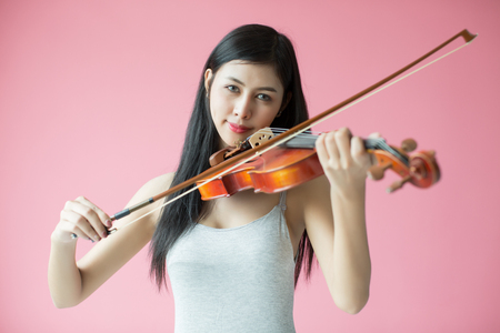 beautiful girl playing the violin on pink backgroundの写真素材