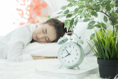 woman asleep in bed while her alarm shows the early time at home in bedroomの写真素材