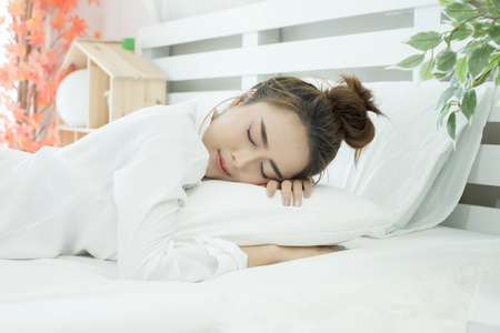 woman asleep in bed while her alarm shows the early time at home in bedroomの写真素材