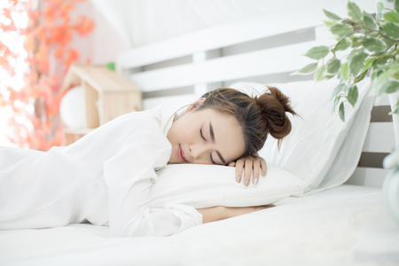 woman asleep in bed while her alarm shows the early time at home in bedroomの写真素材