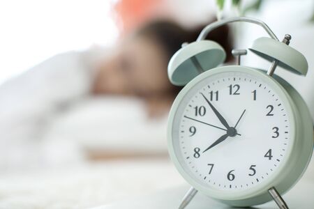 woman asleep in bed while her alarm shows the early time at home in bedroomの写真素材