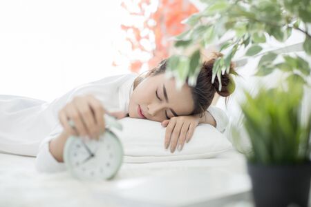 woman asleep in bed while her alarm shows the early time at home in bedroomの写真素材