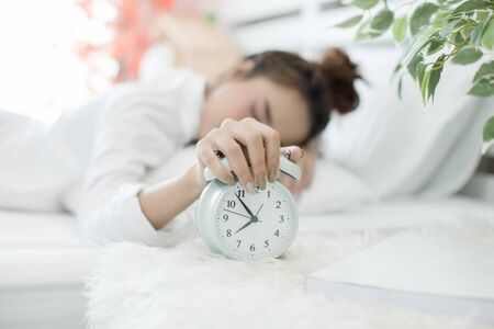 woman asleep in bed while her alarm shows the early time at home in bedroomの写真素材