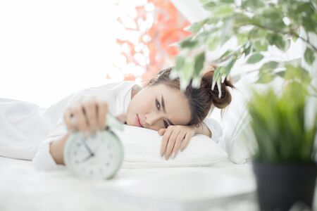 woman asleep in bed while her alarm shows the early time at home in bedroomの写真素材