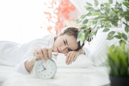 woman asleep in bed while her alarm shows the early time at home in bedroomの写真素材