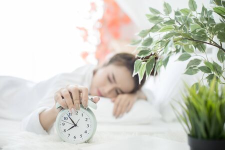 woman asleep in bed while her alarm shows the early time at home in bedroomの写真素材