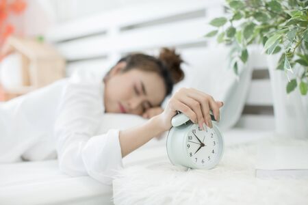 woman asleep in bed while her alarm shows the early time at home in bedroomの写真素材