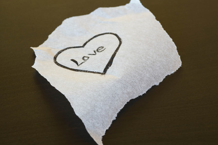 Ripped piece of paper with a drawn black heart in the inside with the word love