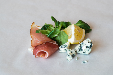Prosciutto ham with blue cheese pieces, decorated with green leafs and lemonの写真素材