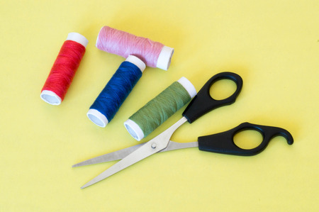 Four pieces of colourful thread rolls with scissors on yellow background