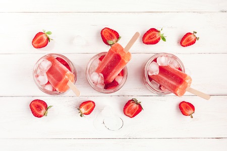 strawberry popsicle, sliced strawberries and ice on a white wooden background, flat lay, top viewの写真素材