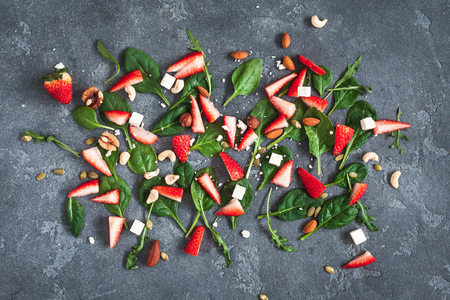 Ingredients for strawberry salad. Spinach leaves, sliced strawberries, nuts, feta cheese on kitchen blackboard. Healthy food concept. Fat lay, top viewの写真素材