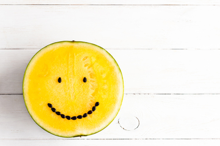 jellow watermelon with smile on white wooden background, top view, flat layの写真素材