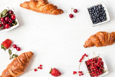 croissant, blueberry, cherry and red currant on white wooden background, breakfast, top view, flat layの写真素材