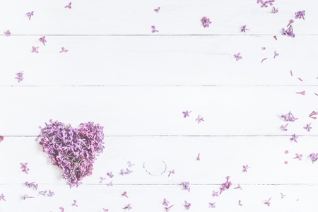 Spring flowers. lilac flowers in the shape of heart on white wooden background, top view, flat layの写真素材
