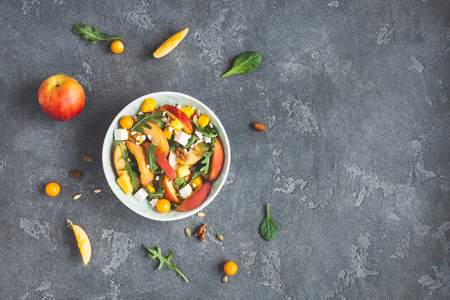 Peach salad. Spinach leaves, arugula, sliced peaches, mango, nuts, feta cheese on black background. Fruit salad. Flat lay, top view, copy spaceの写真素材
