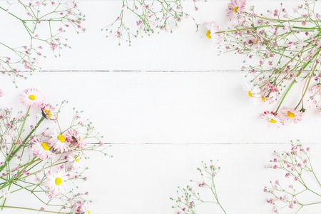 Flowers composition. Floral frame made of pink gypsophila flowers and daisy flowers on white wooden background. Flat lay, top view, copy spaceの写真素材