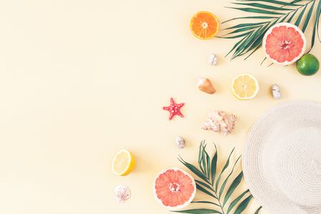 Summer composition. Fruits, hat, tropical palm leaves, seashells on pastel yellow background. Summer concept. Flat lay, top view, copy spaceの写真素材