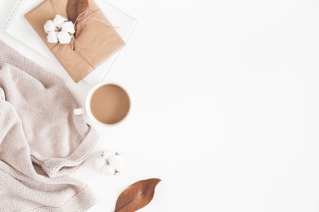 Autumn or winter composition. Cup of coffee, gift, dried autumn leaves, beige sweater on white background. Flat lay, top view, copy spaceの写真素材