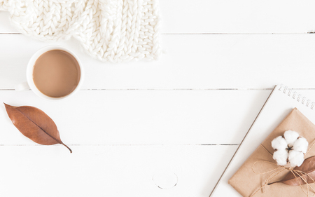 Autumn or winter composition. Cup of coffee, gift, dried autumn leaves, knitted blanket on white wooden background. Flat lay, top view, copy spaceの写真素材