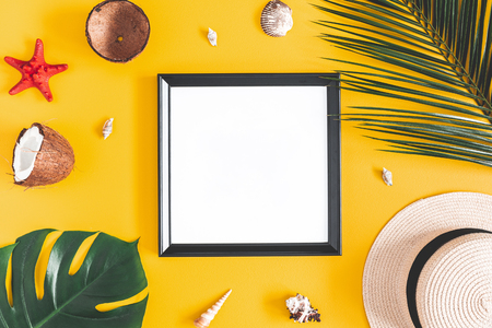 Summer composition. Tropical palm leaves, photo frame, coconut, hat on yellow background. Summer, nature concept. Flat lay, top view, copy spaceの写真素材