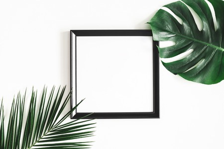 Summer composition. Tropical palm leaves, black photo frame on white background. Summer, nature...