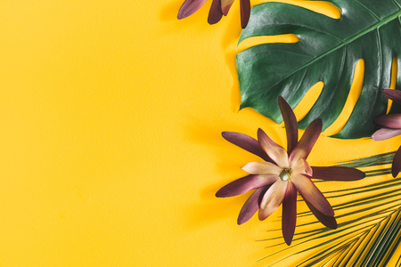 Summer composition. Tropical palm leaves and flowers on yellow background. Summer concept. Flat lay, top view, copy spaceの写真素材