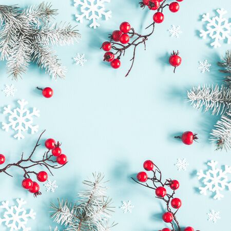 Christmas or winter composition. Frame made of snowflakes, fir tree branches and red berries on pastel blue background. Christmas, winter, new year concept. Flat lay, top view, copy space, squareの写真素材