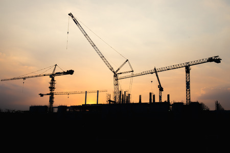 Industrial construction crane working and building at site on sunset timeの写真素材