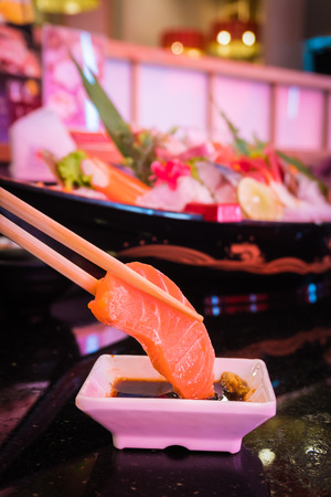 Closeup of hand with wooden chopsticks and salmon raw dip shoyu or japanese sauce and wasabi. Select focusの写真素材